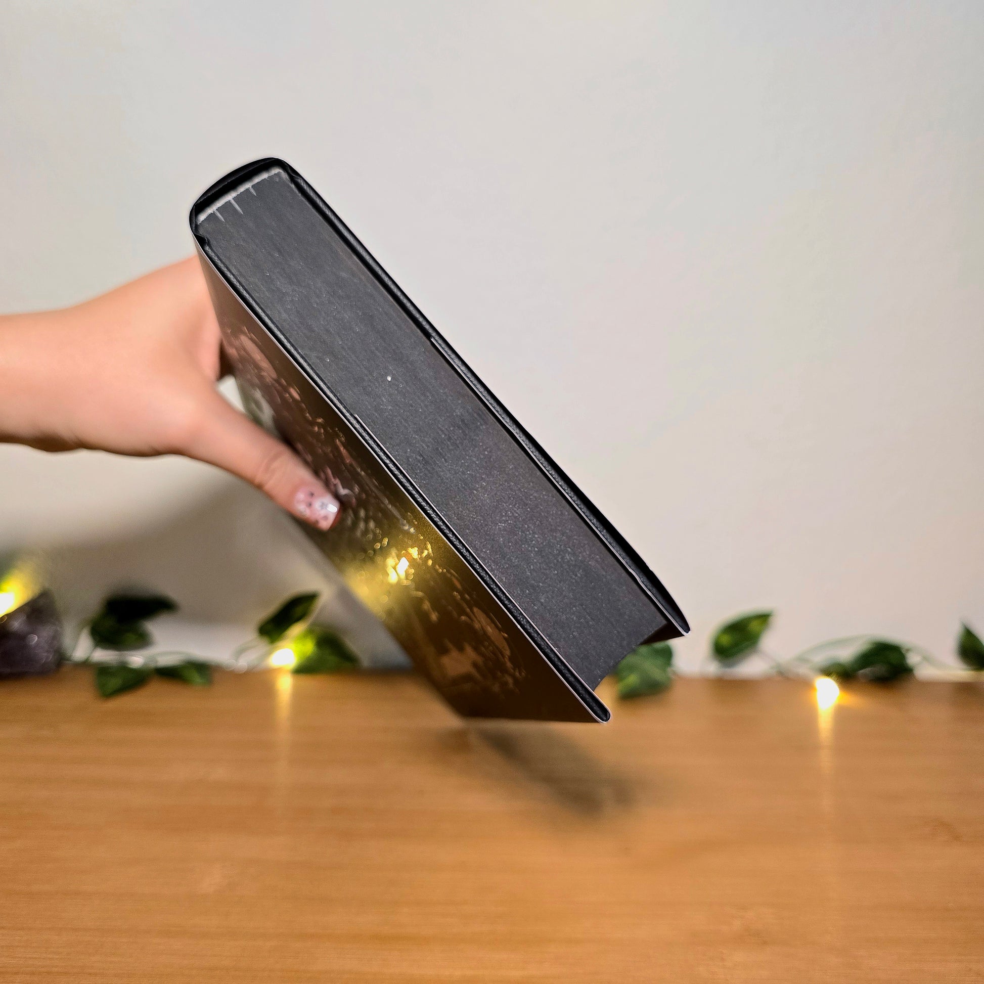 Hand holding a black rectangular object on a wooden surface with a blurred background