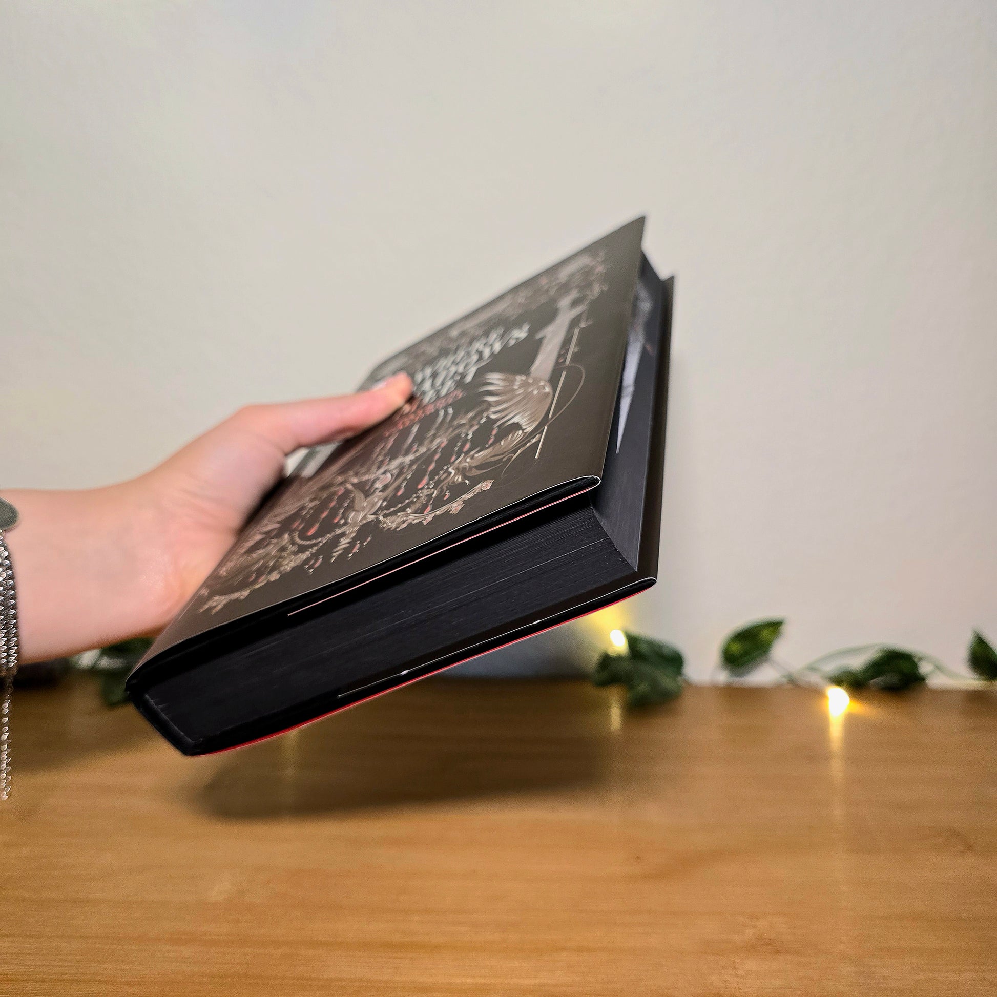 Person holding a black book with intricate design on a wooden surface
