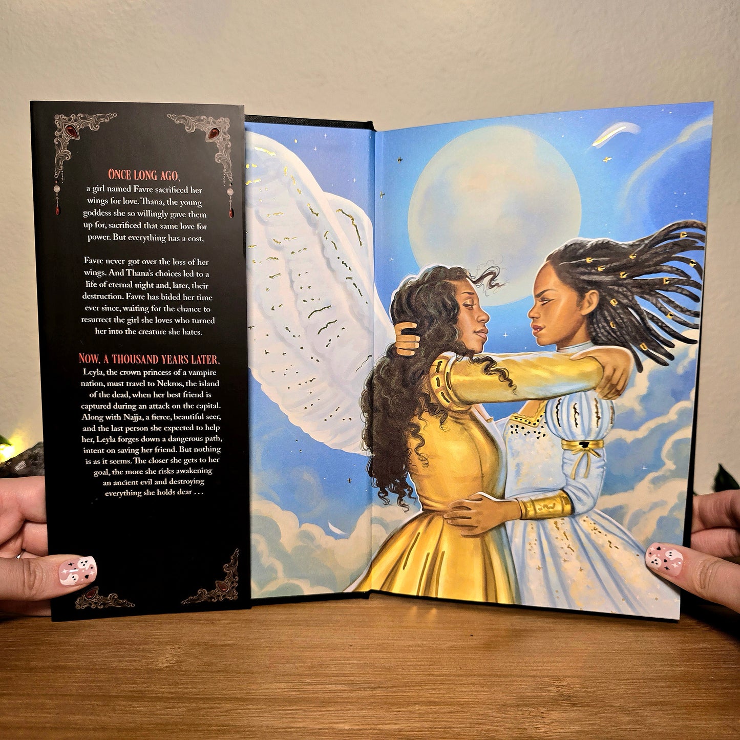 Open book showing two women embracing with angel wings against a celestial background