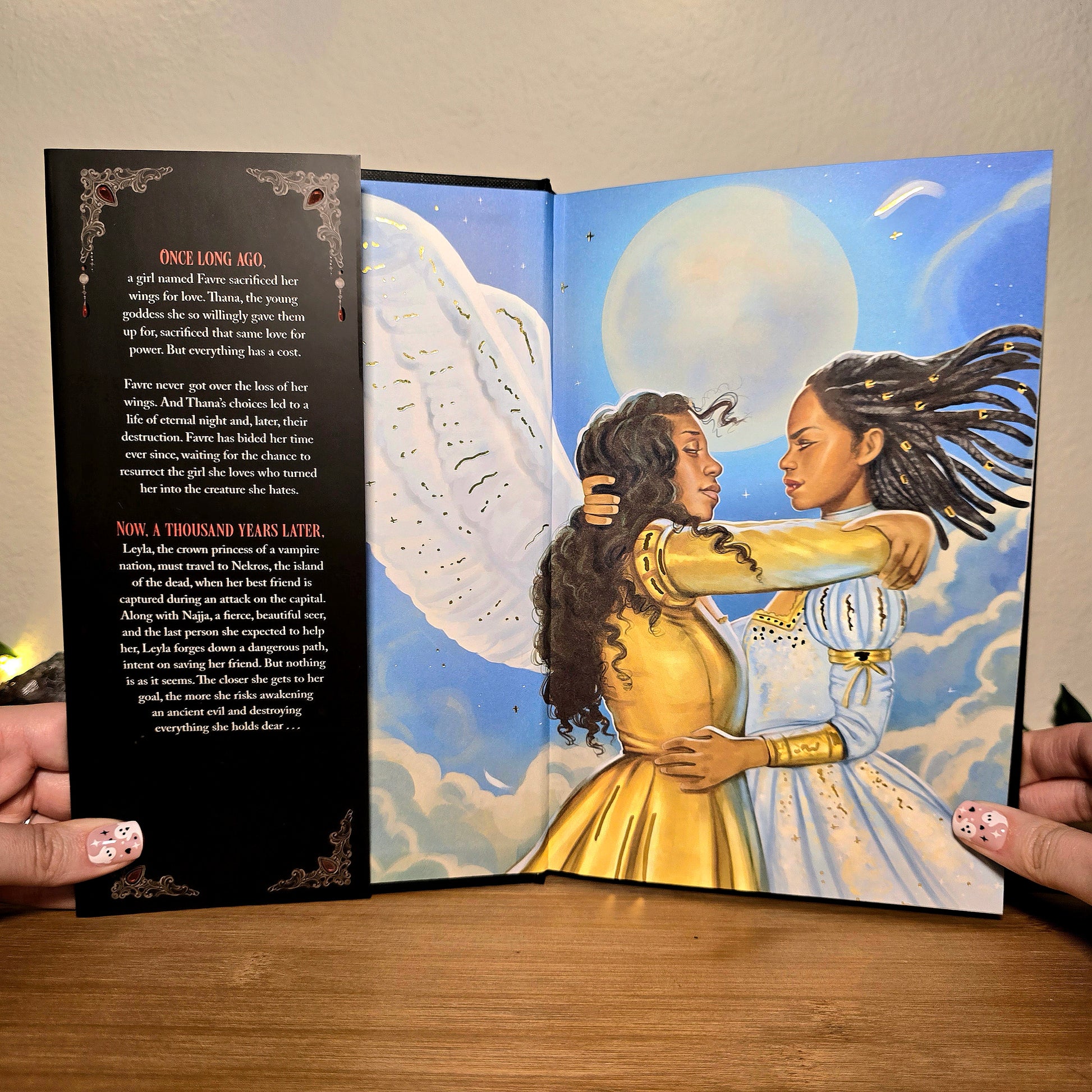 Open book showing two women embracing with angel wings against a celestial background