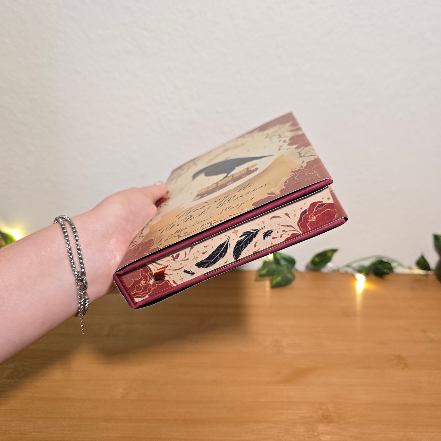 Hand holding a decorative box with floral designs against a wooden background