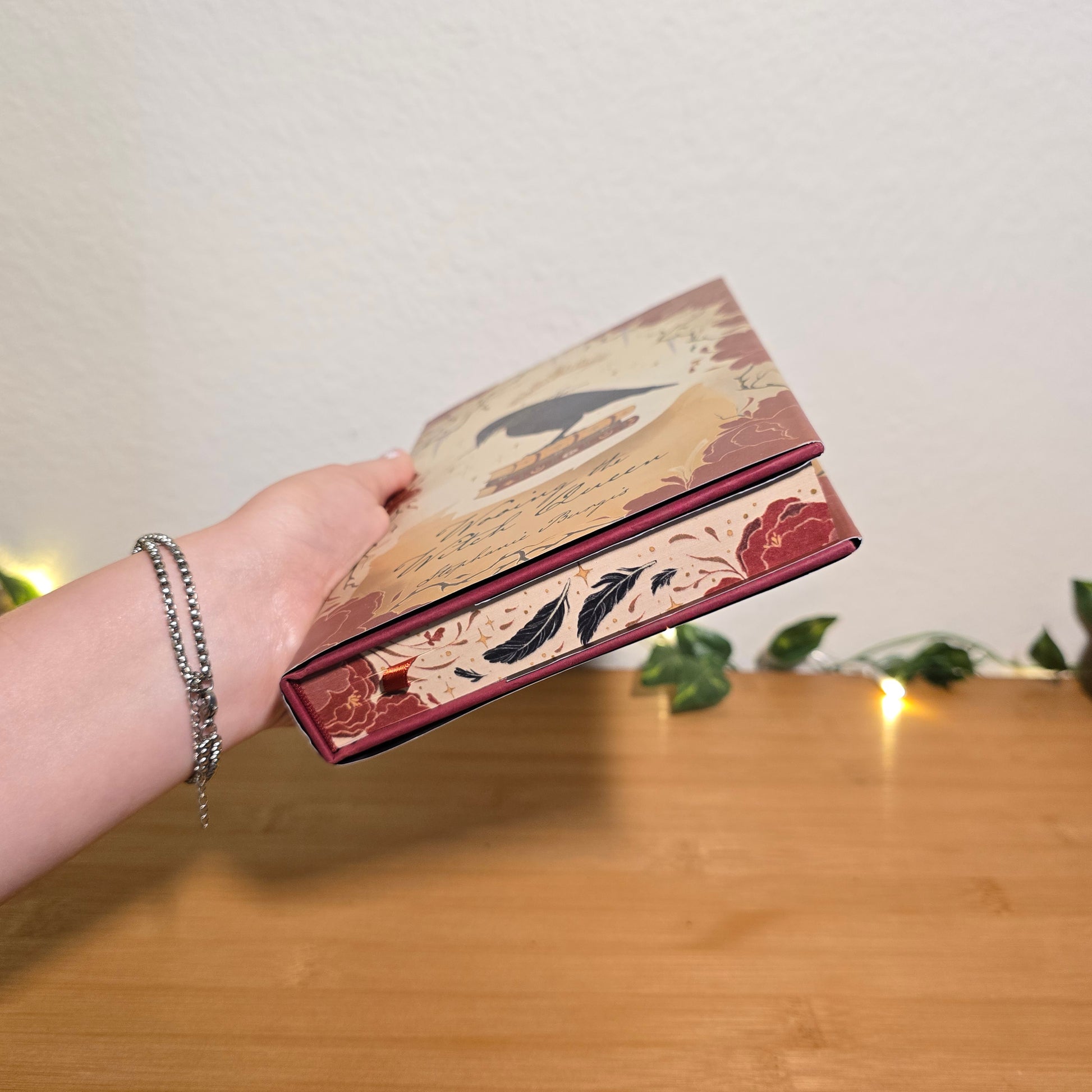 Hand holding a decorative box with floral designs against a wooden background