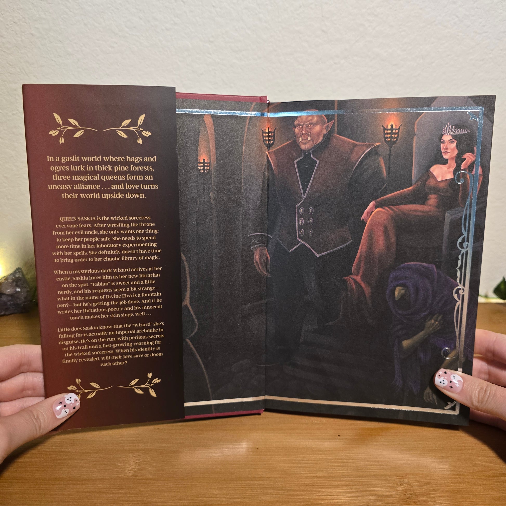 Open book with a dark cover featuring an illustration of a woman and a man, held by a person on a wooden surface.